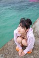 A woman sitting on a rock by the water.