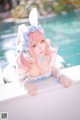 A woman with pink hair and bunny ears sitting by a pool.