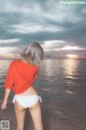 A woman in a red shirt and white bikini standing on a beach.