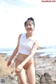 A woman in a bikini standing on a rock by the ocean.