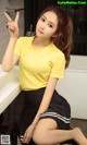 A woman in a yellow shirt and black skirt posing for a picture.