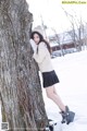 A woman leaning against a tree in the snow.