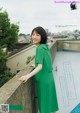 A woman in a green dress leaning against a wall.